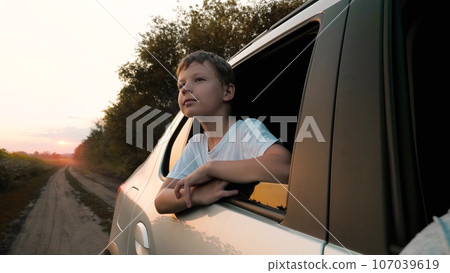Dreaming little boy leans out of car window while riding along rural road Dreaming little boy leans out of car window while riding along rural road 107039619