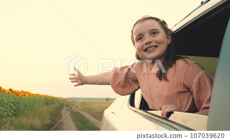 Laughing little girl puts hand out of car window driving along rural road Laughing little girl puts hand out of car window driving along rural road 107039620
