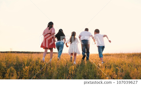 Sportive parents with little children run across grassy field to horizon in summer 107039627