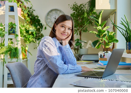 Portrait of young woman sitting at home at desk with computer laptop 107040008