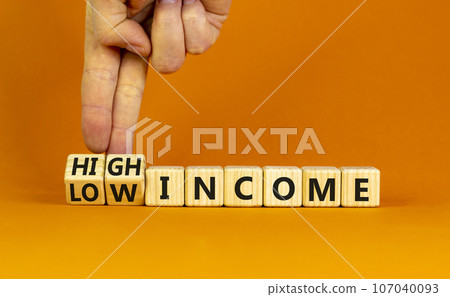 Low or high income symbol. Businessman turns wooden cubes and changes words Low income to High income. Beautiful orange table orange background, copy space. Business low or high income concept. 107040093
