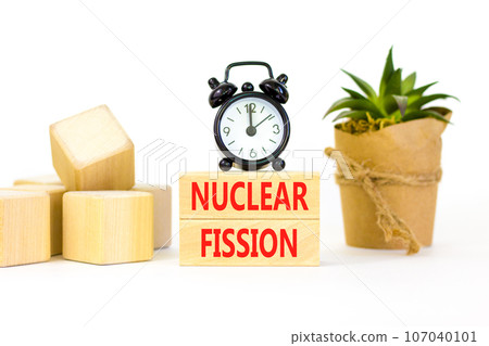Nuclear fission symbol. Concept words Nuclear fission on beautiful wooden blocks. Beautiful white table white background. Black alarm clock. Business science nuclear fission concept. Copy space. 107040101
