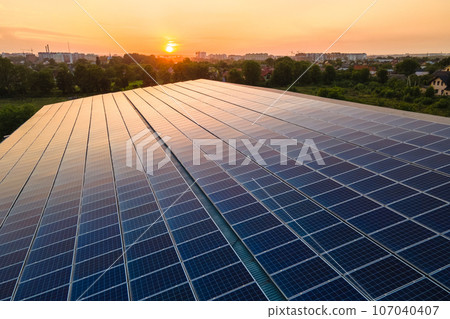 Blue photovoltaic solar panels mounted on building roof for producing clean ecological electricity at sunset. Production of renewable energy concept. Blue photovoltaic solar panels mounted on building roof for producing clean ecological electricity at sunset. Production of renewable energy concept. 107040407