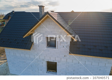 Aerial view of unfinished house with aerated lightweight concrete walls and wooden roof frame covered with metallic tiles under construction. 107040571