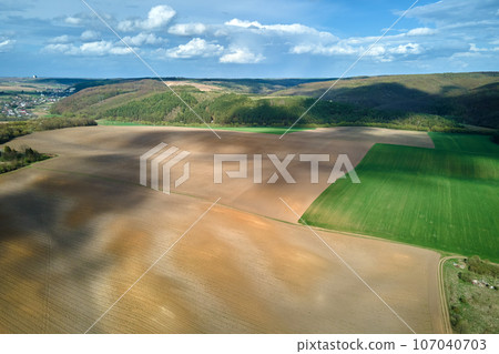 Aerial view of plowed agricultural fields with cultivated fertile soil prepared for planting crops between green woods in spring 107040703