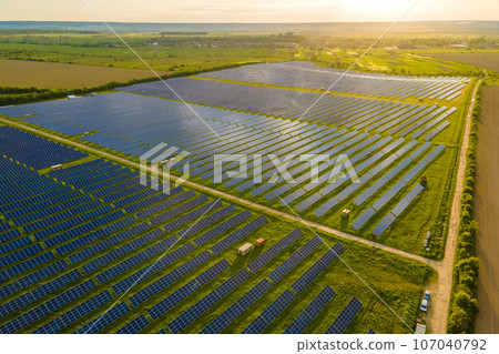 Aerial view of large electrical power plant with many rows of solar photovoltaic panels for producing clean ecological electric energy at sunrise. Renewable electricity with zero emission concept Aerial view of large electrical power plant with many rows of solar photovoltaic panels for producing clean ecological electric energy at sunrise. Renewable electricity with zero emission concept 107040792