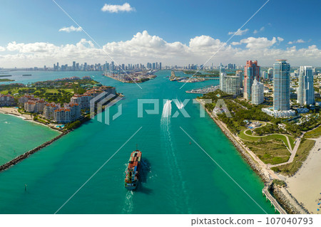 Aerial view of large container ship entering in Miami harbor main channel near South Beach. Luxurious hotels and apartment buildings on waterfront and high skyscrapers of downtown district in distance 107040793