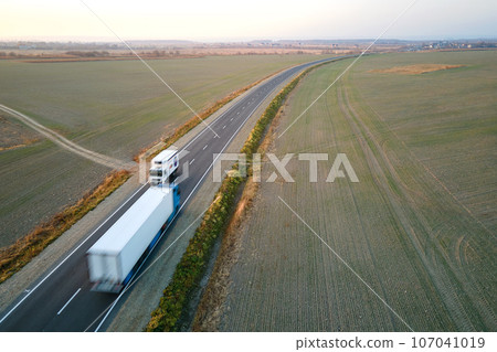 Aerial view of cargo trucks driving on highway hauling goods. Delivery transportation and logistics concept Aerial view of cargo trucks driving on highway hauling goods. Delivery transportation and logistics concept 107041019