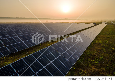 Aerial view of big sustainable electric power plant with many rows of solar photovoltaic panels for producing clean electrical energy at sunset. Renewable electricity with zero emission concept Aerial view of big sustainable electric power plant with many rows of solar photovoltaic panels for producing clean electrical energy at sunset. Renewable electricity with zero emission concept 107041061