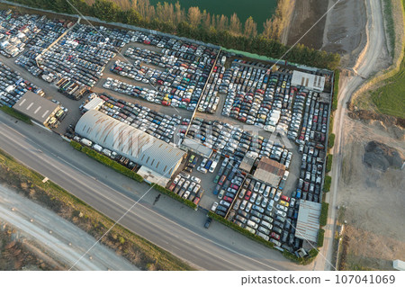 Aerial view of big parking lot of junkyard with rows of discarded broken cars. Recycling of old vehicles Aerial view of big parking lot of junkyard with rows of discarded broken cars. Recycling of old vehicles 107041069