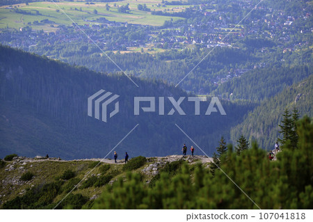 Amidst the breathtaking Tatra Mountains, Poland, hikers traverse scenic trails, immersed in the awe-inspiring beauty of nature's grandeur. With each step, they embrace the serene adventure 107041818