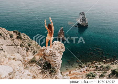 Woman travel sea. Happy tourist enjoy taking picture outdoors for memories. Woman traveler looks at the edge of the cliff on the sea bay of mountains, sharing travel adventure journey Woman travel sea. Happy tourist enjoy taking picture outdoors for memories. Woman traveler looks at the edge of the cliff on the sea bay of mountains, sharing travel adventure journey 107042052