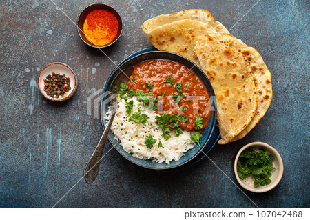 Traditional Indian Punjabi dish Dal makhani with lentils and beans in black bowl served with basmati rice, naan flat bread, fresh cilantro and spoon on blue concrete rustic table top view Traditional Indian Punjabi dish Dal makhani with lentils and beans in black bowl served with basmati rice, naan flat bread, fresh cilantro and spoon on blue concrete rustic table top view 107042488
