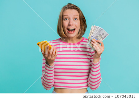 Young woman use smartphone rejoicing win, receiving money dollar cash banknotes, celebrating success Young woman use smartphone rejoicing win, receiving money dollar cash banknotes, celebrating success 107043015