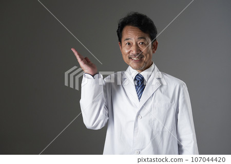 Middle-aged doctor pointing to the left side with the palm of his hand, black background 107044420