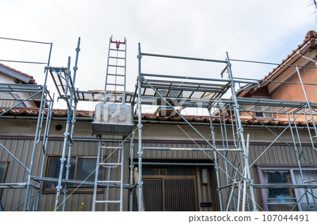 Scaffolding installed to replace roof tiles of an old detached house | Roof renovation image | Tile renovation image Scaffolding installed to replace roof tiles of an old detached house | Roof renovation image | Tile renovation image 107044491