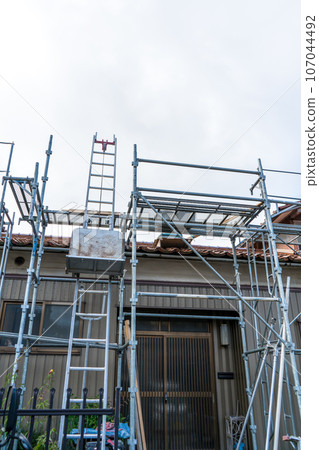 Scaffolding installed to replace roof tiles of an old detached house | Roof renovation image | Tile renovation image Scaffolding installed to replace roof tiles of an old detached house | Roof renovation image | Tile renovation image 107044492