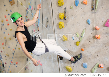 Confident young man wearing helmet scaling artificial climbing wall in climbing gym Confident young man wearing helmet scaling artificial climbing wall in climbing gym 107045156