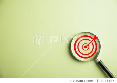 The magnifier glass centers on a target board, signifying focused business objectives., it represents the concept of search, goal attainment, strategic planning, and marketing success. 107045387