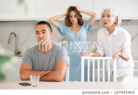 Elderly woman quarrels with couple in kitchen 107045403