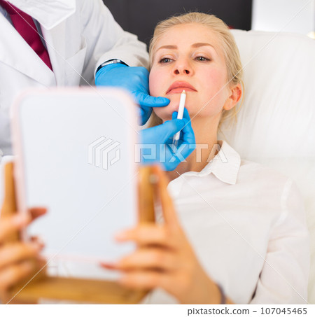 Cosmetologist hands making marks on face of female patient prior to surgery 107045465