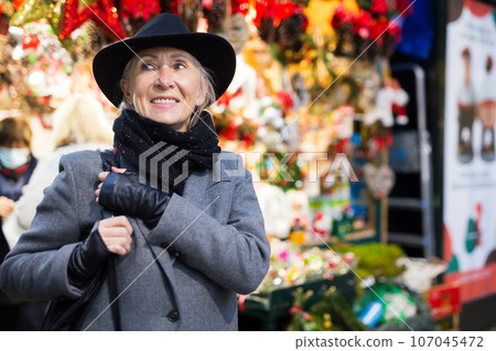 Smiling aged woman walking at traditional city christmas fair 107045472