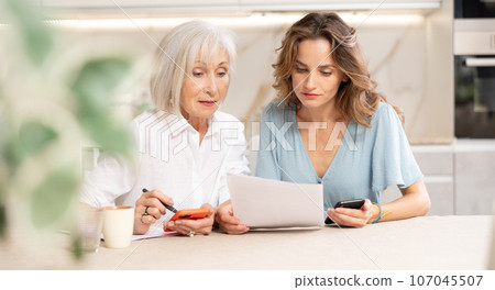 Adult woman and elderly woman discussing agreement in kitchen 107045507