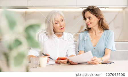 Adult woman and elderly woman discussing agreement in kitchen 107045508