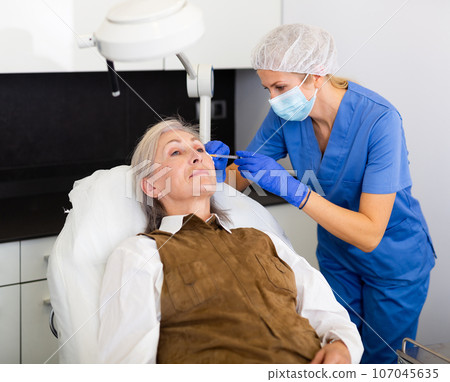 Cosmetologist doing botulotoxin injections for senior woman 107045635
