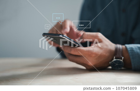 Modern connectivity man on phone types, discussing live chat and social network concepts. Home office with chat box icons portrays digital communication trends. Social media marketing technology 107045809