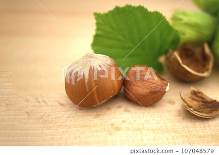 Unshelled and cracked hazelnuts near green leaves Unshelled and cracked hazelnuts near green leaves 107048579