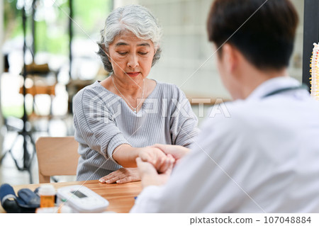 An Asian retired old lady is being checked for pulse on her wrist by a doctor at a hospital. An Asian retired old lady is being checked for pulse on her wrist by a doctor at a hospital. 107048884