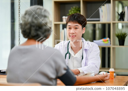 A professional Asian male doctor is diagnosing the disease and consulting with an old lady. A professional Asian male doctor is diagnosing the disease and consulting with an old lady. 107048895