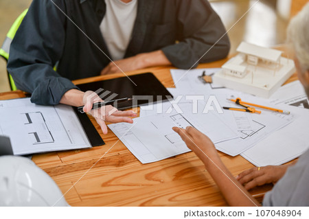A male architect or interior designer is consulting on building plans and designs with a client. 107048904
