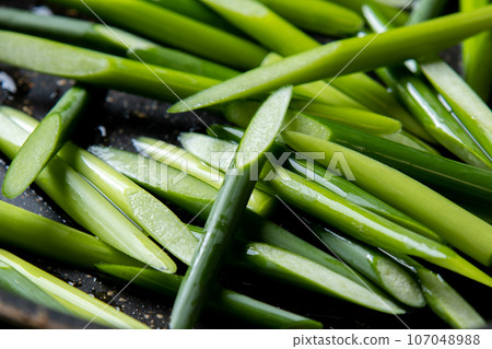 A cooking scene where garlic sprouts (diagonally cut) are fried in a frying pan. 107048988