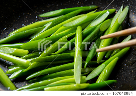 A cooking scene where garlic sprouts (diagonally cut) are fried in a frying pan. A cooking scene where garlic sprouts (diagonally cut) are fried in a frying pan. 107048994