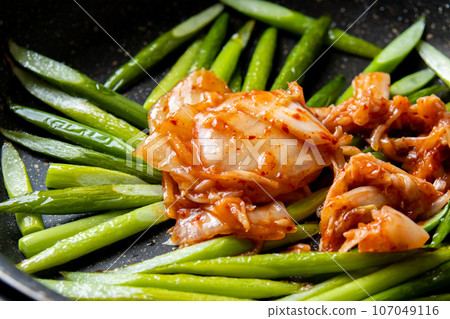 A cooking scene in which garlic sprouts (cut diagonally) and Chinese cabbage kimchi are stir-fried in a frying pan. 107049116