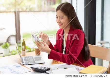An attractive Asian businesswoman using her smartphone at her desk. 107050274