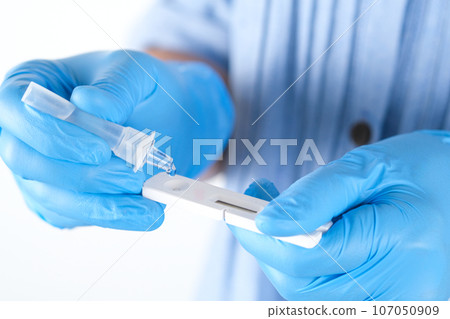 The doctor holds a COVID-19 swab collection, wears blue gloves and a PPE protective mask, and carries a test tube to collect the OP NP and test coronavirus. 107050909