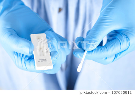 The doctor holds a COVID-19 swab collection, wears blue gloves and a PPE protective mask, and carries a test tube to collect the OP NP and test coronavirus. 107050911