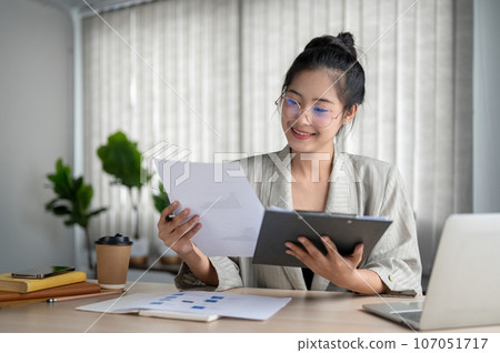A satisfied and professional Asian businesswoman examines business reports at her desk. 107051717