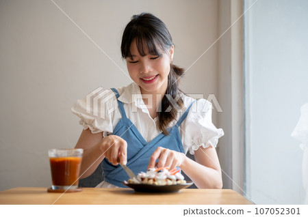 A pretty Asian woman enjoys eating a croissant waffle and an iced coffee in a coffee shop alone. 107052301
