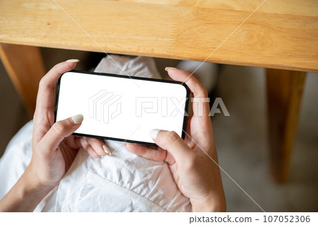 Close-up image of a woman playing a mobile game while relaxing in a coffee shop. Close-up image of a woman playing a mobile game while relaxing in a coffee shop. 107052306