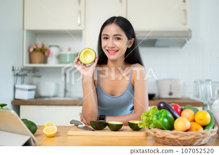 A woman shows an avocado to the camera while she prepares her healthy meals in the kitchen. A woman shows an avocado to the camera while she prepares her healthy meals in the kitchen. 107052520