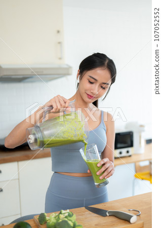 A happy Asian woman in gym clothes is making her healthy breakfast in the kitchen after a workout. 107052552