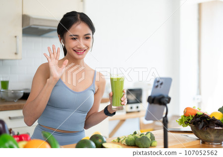 A beautiful Asian female online nutrition coach is live streaming while making her morning smoothie. 107052562