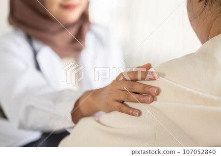 A caring Asian Muslim female doctor is touching a patient's shoulder to reassure her. 107052840