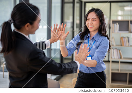 A cheerful Asian businesswoman is giving high fives to her colleague. Teamwork, team building A cheerful Asian businesswoman is giving high fives to her colleague. Teamwork, team building 107053450