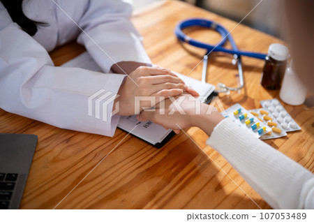 Close-up image of a doctor holding a patient's hand to reassure her during a medical checkup. Close-up image of a doctor holding a patient's hand to reassure her during a medical checkup. 107053489