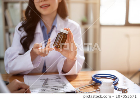 A professional Asian female doctor is describing pills to a patient. cropped image 107053571